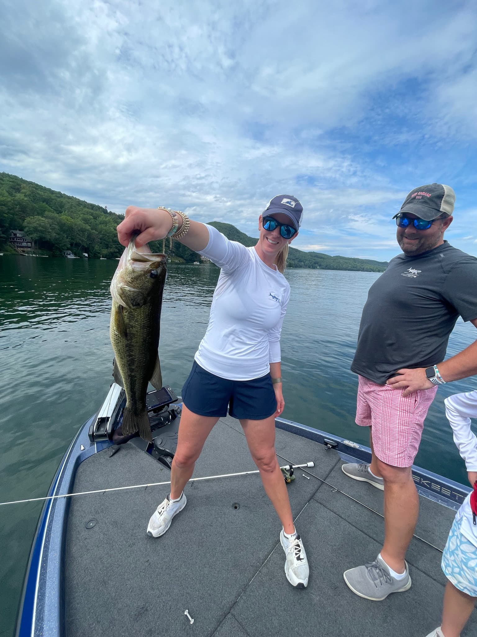 Woman in white shirt next to man holding largemouth bass on blue boat