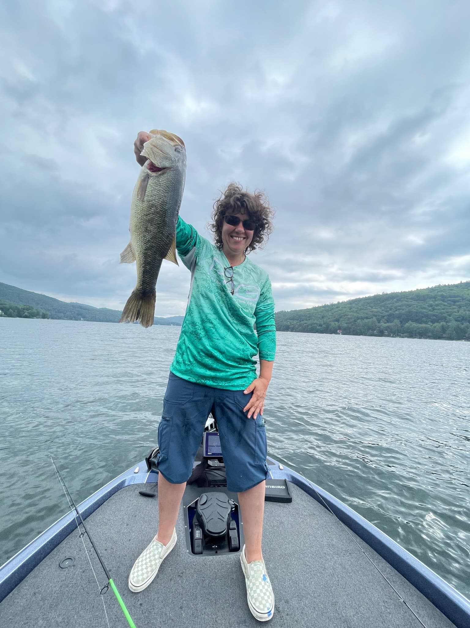 Older woman in green shirt holds laremouth bass on blue boat