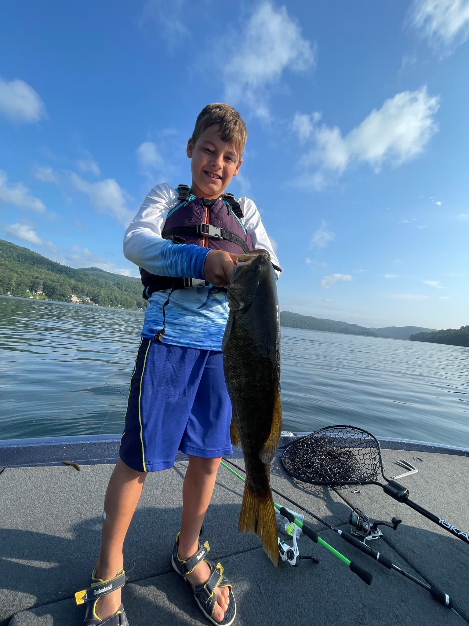 boy in purple life jacket holds smallmouth bass with two hands