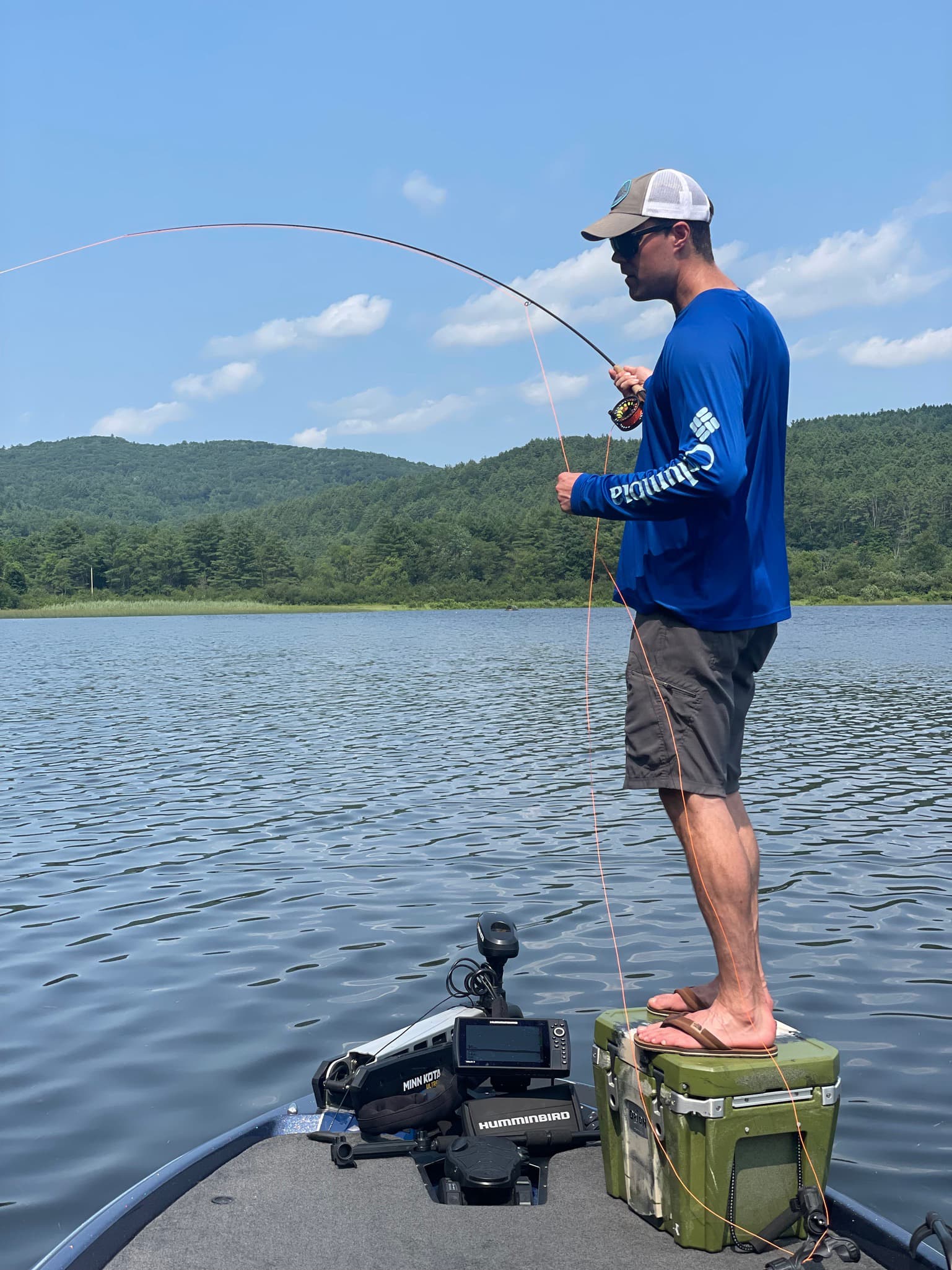 Man in blue shirt standing on green cooler fly fishing on boat