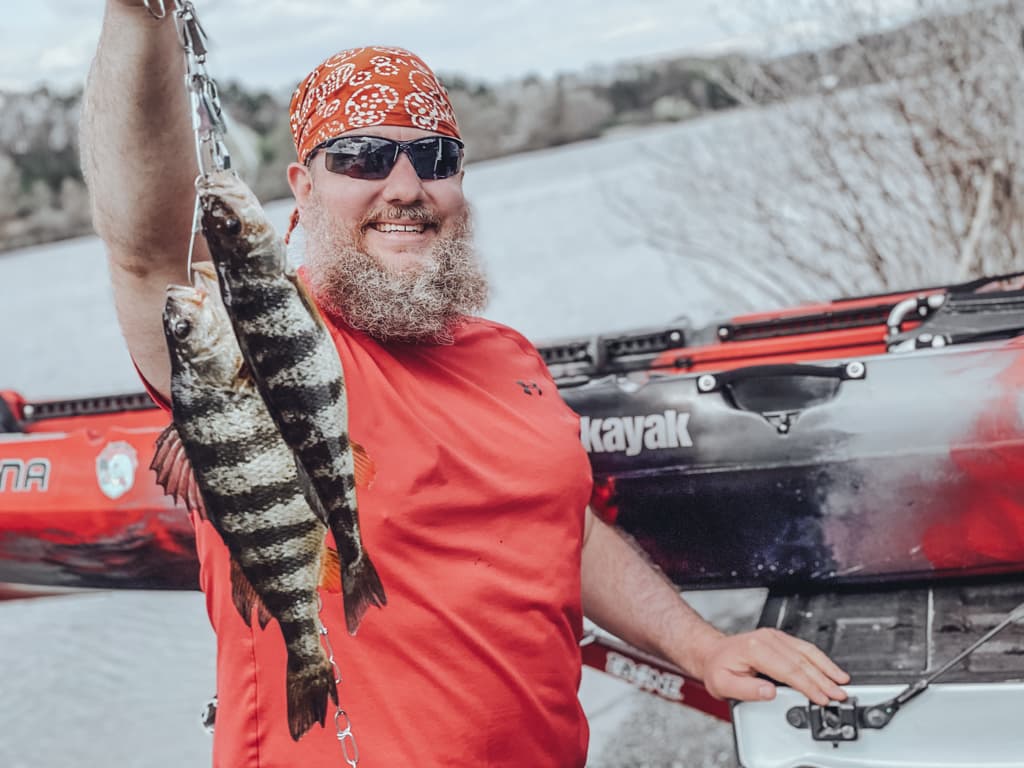 Man in red shirt holding two fish while smiling