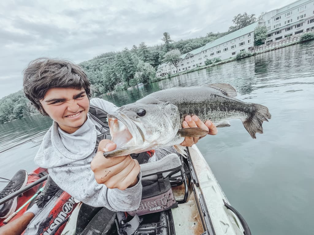 Young man in grey sweatshirt holding one fish while smirking in kayak