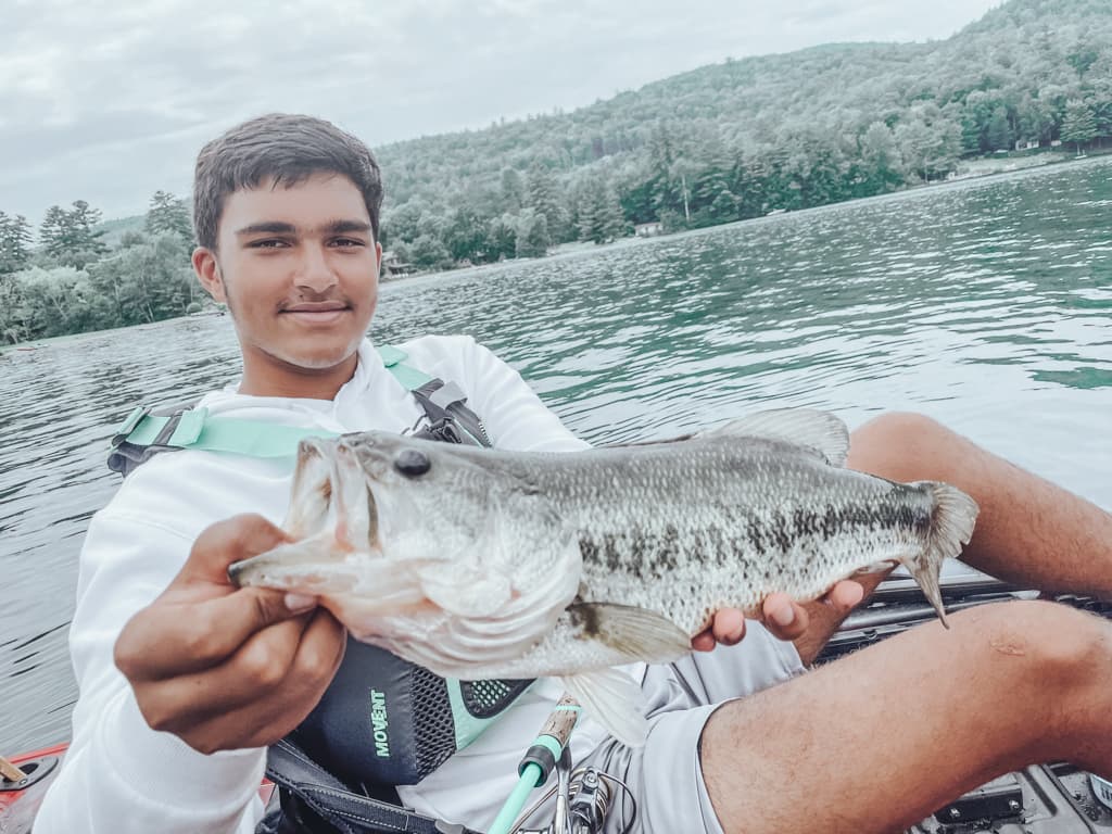 Young man in white sweatshirt holding one fish while smiling in kayak