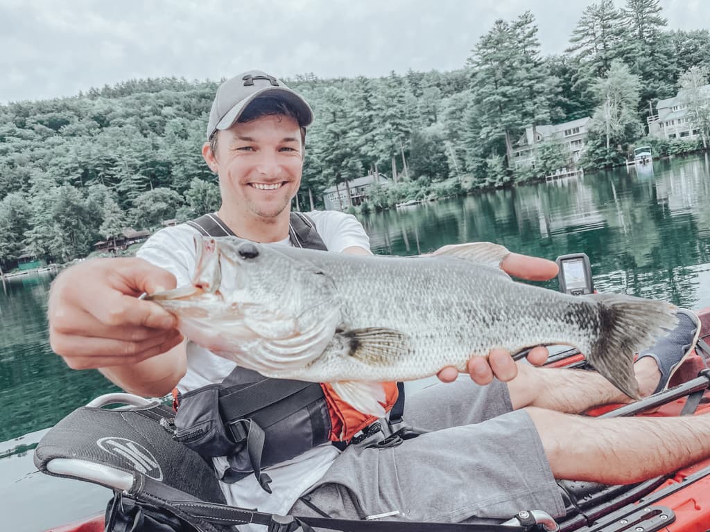 Man in white shirt holding one fish while smiling in kayak