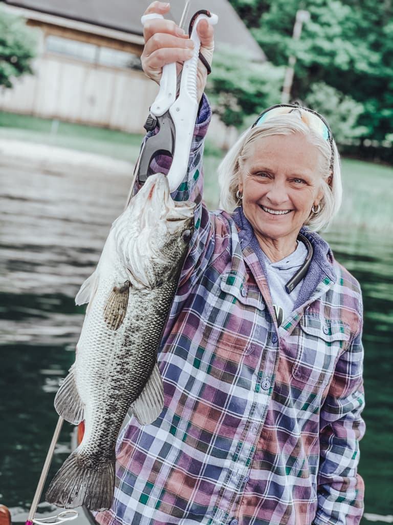 Older woman in a flannel jacket holding one fish while smiling
