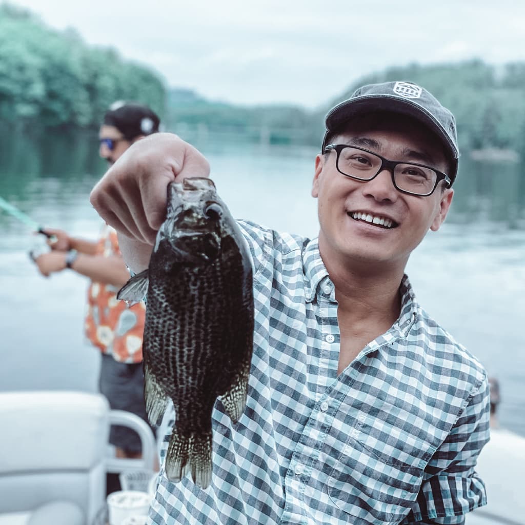 Man in a button-down shirt, glasses, and hat holding a wish while smiling on a boat