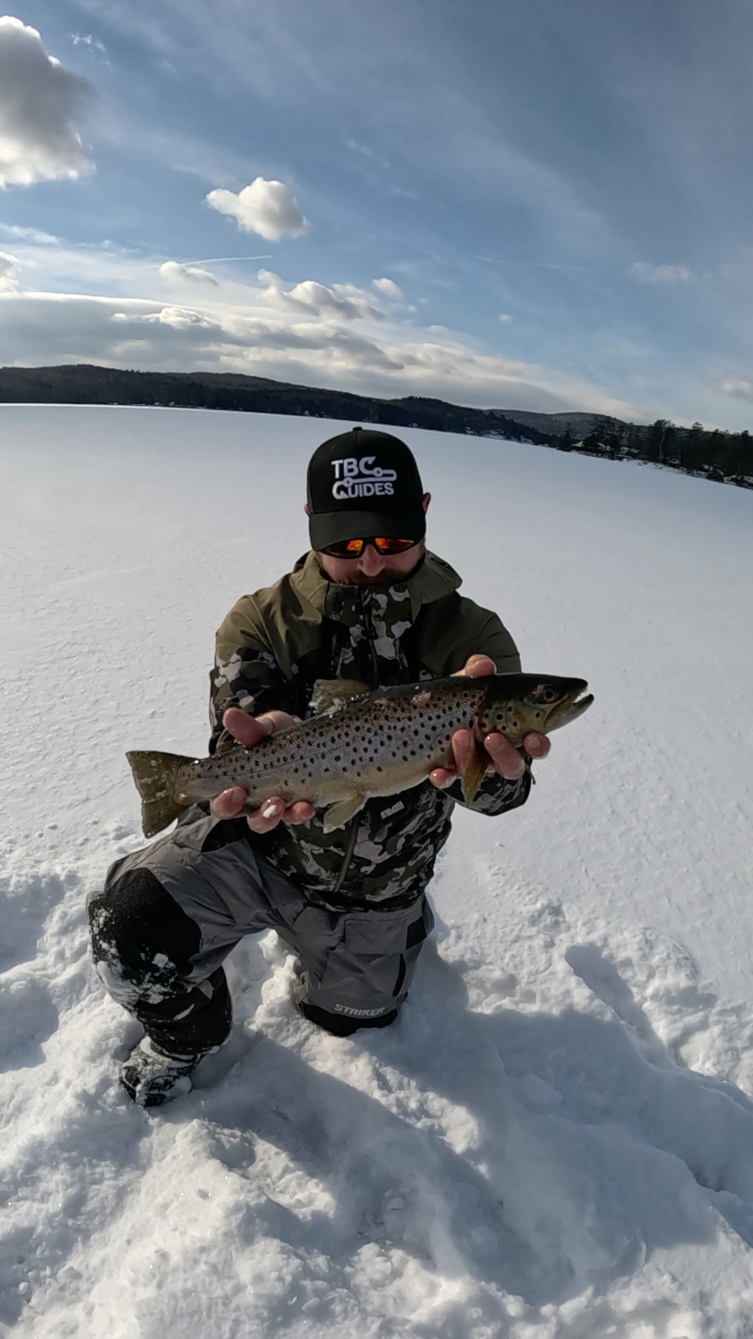 Man kneeling on frozen lake while holding fish horizontally
