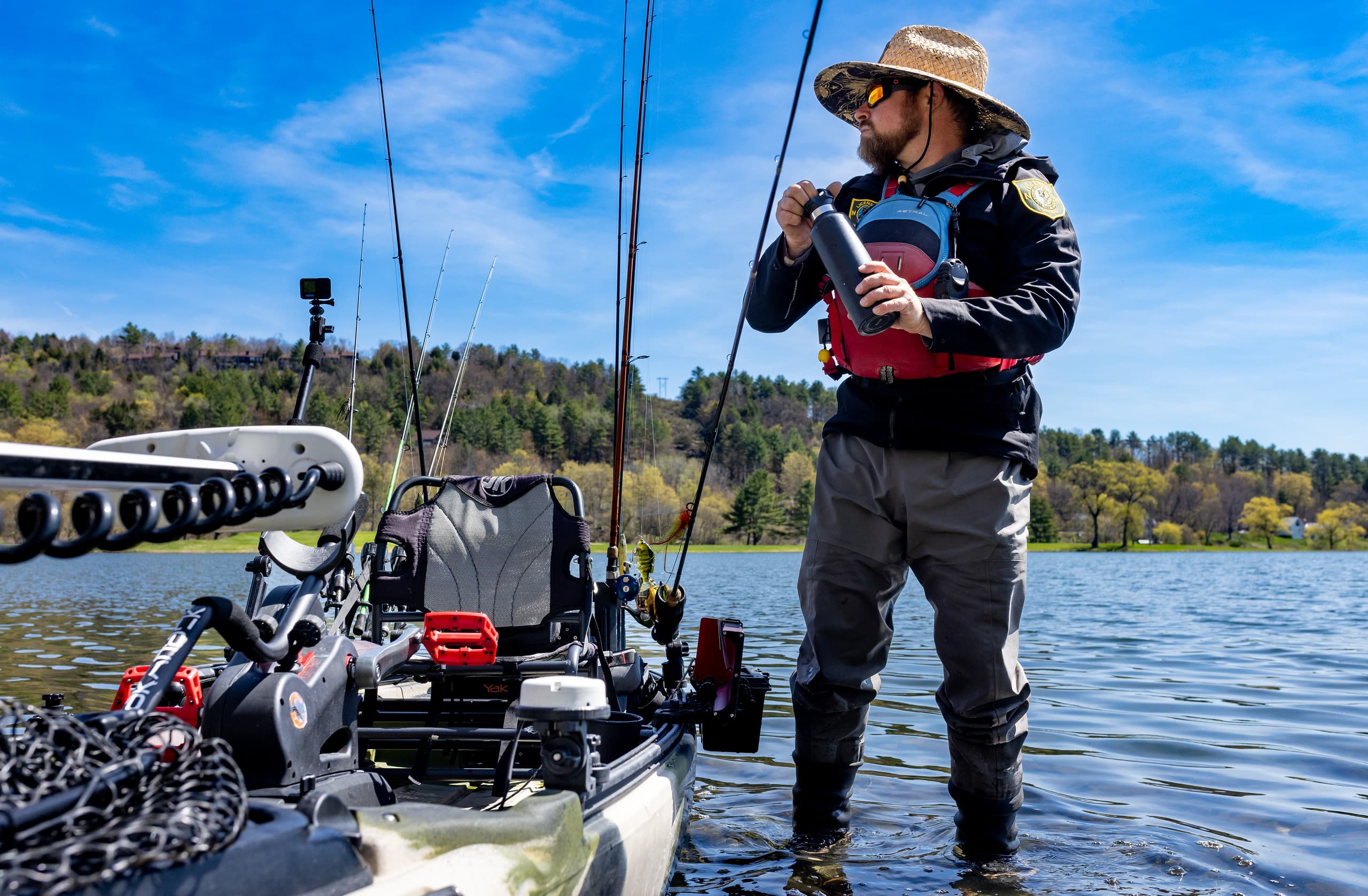 man standing in water beside kayak fishing boat holding black water bottle