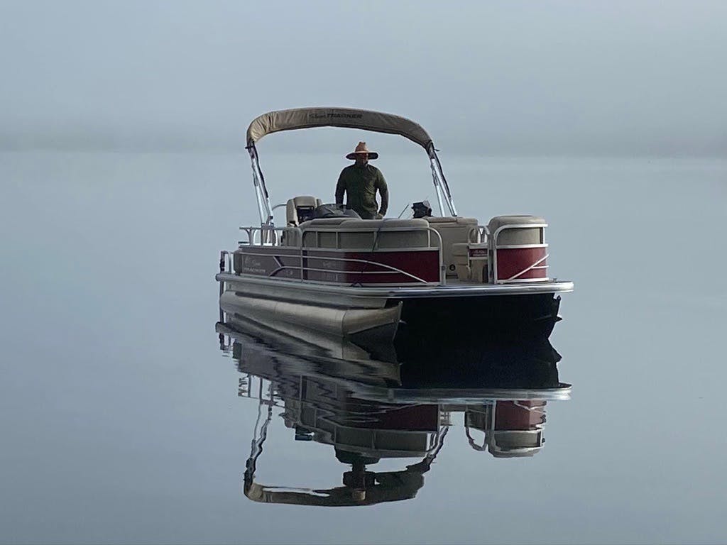 Man standing on a red and white pontoon boat in the middle of a foggy lake 