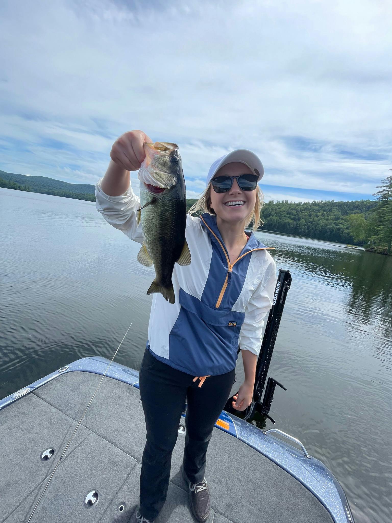 Woman in white hat and black pants holding largemouth bass