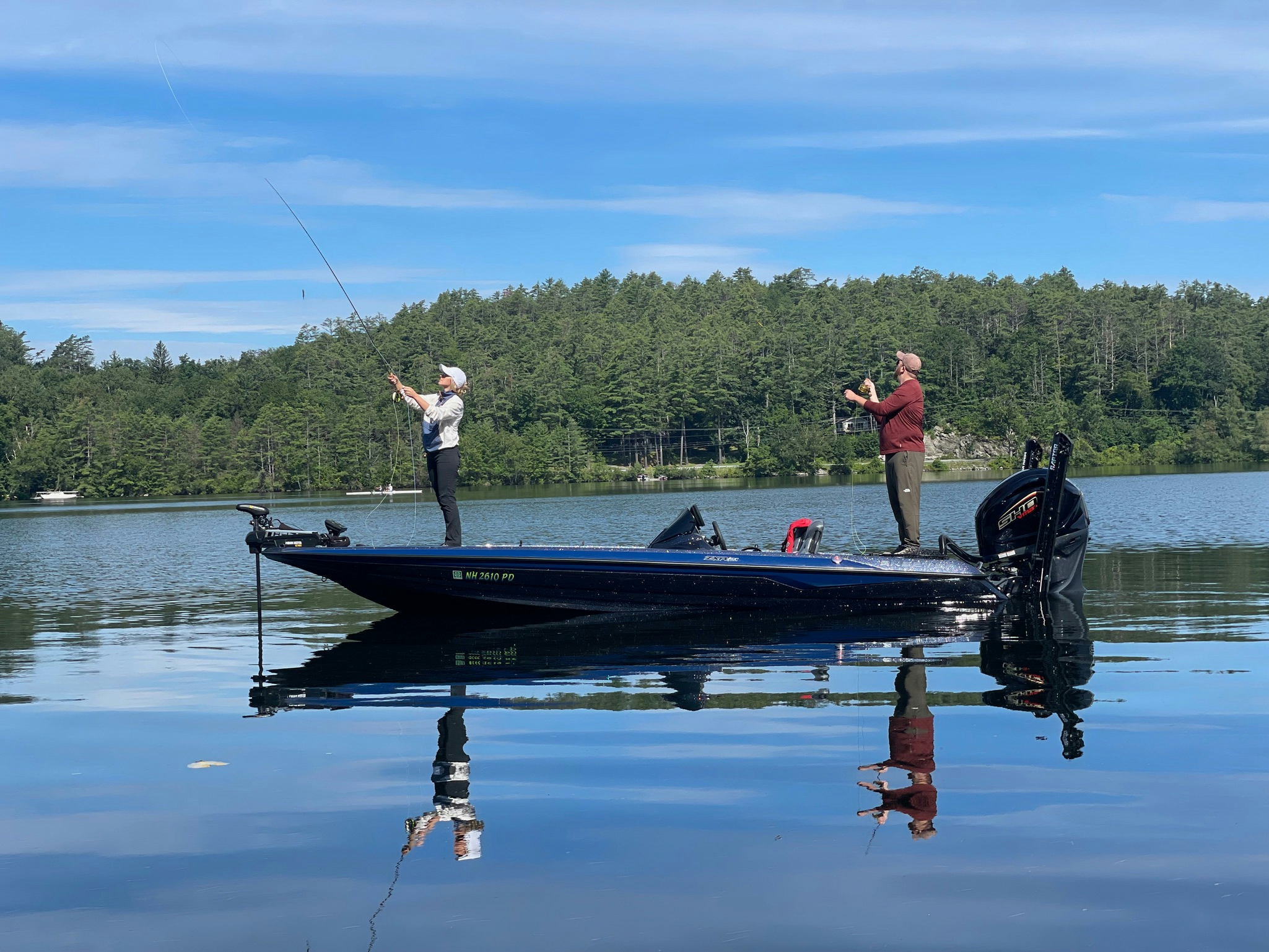 Man in red shirt and woman in white jacket and blank pants fly fishing on blue boat