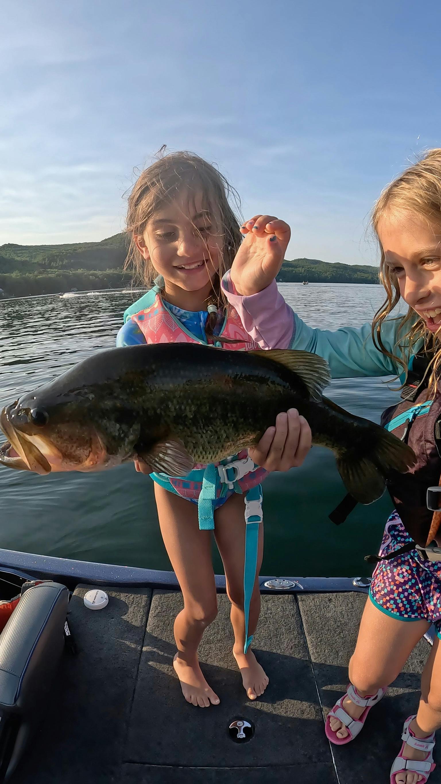 Two girls in swimsuits hold largemouth bass on blue boat