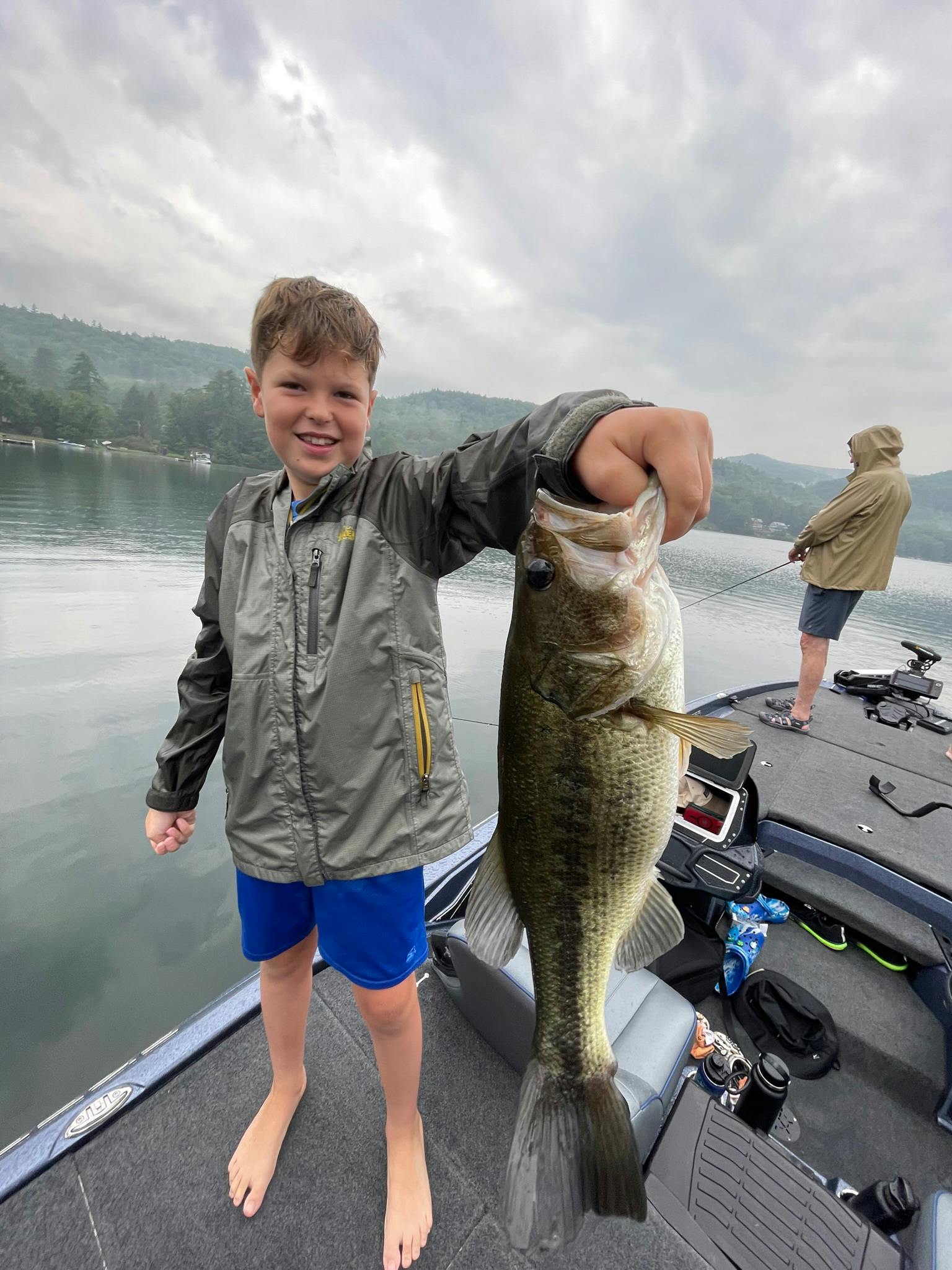 boy in grey jacket holds largemouth bass on blue boat