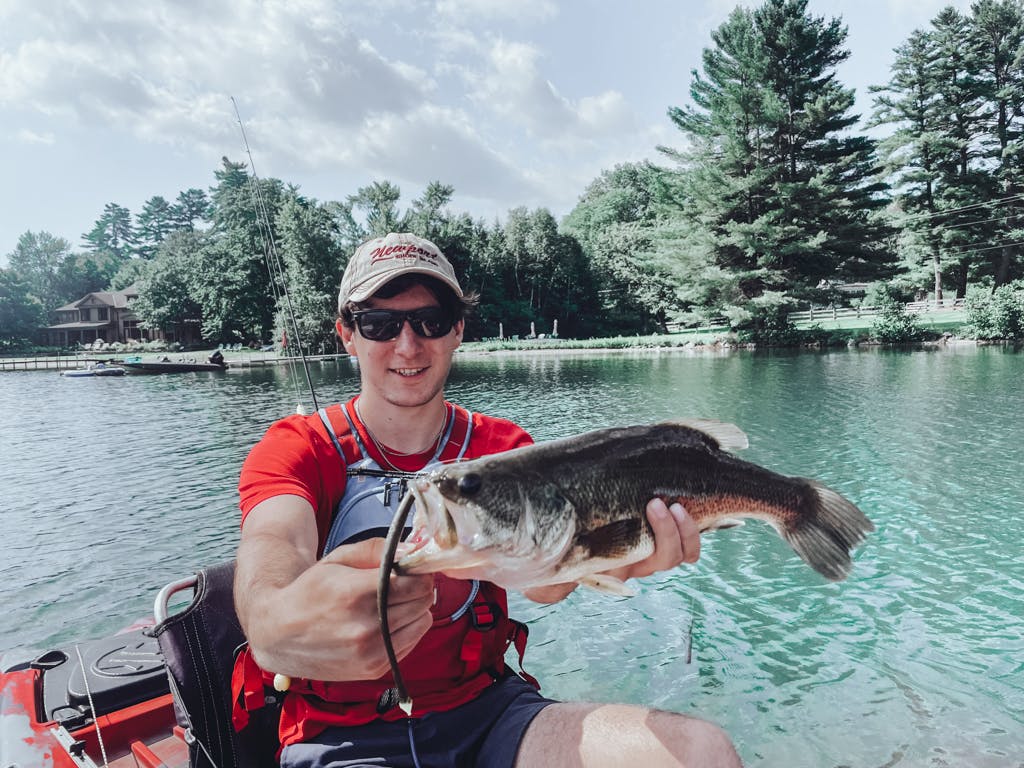 Young man in red T-shirt and beige hat holding one fish while smiling in kayak