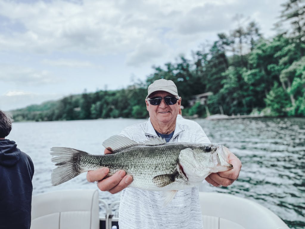 Older man in white shirt and beige American hat holding one fish while smiling on boat