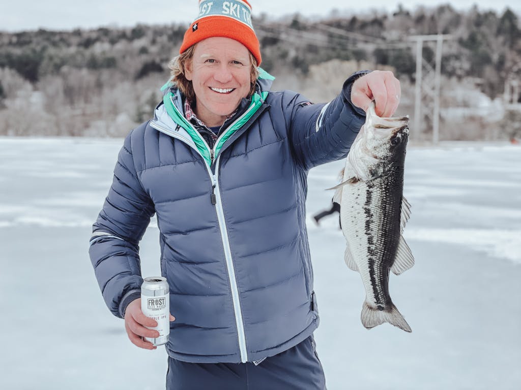 Man with orange hat holding a fish on a frozen lake while smiling