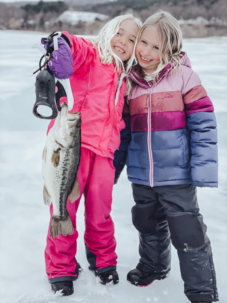 Two young girls in large coats holding a fish while smiling
