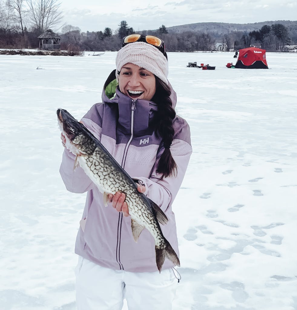 Middle-aged woman in a purple jacket holding a fish on a frozen lake while smiling