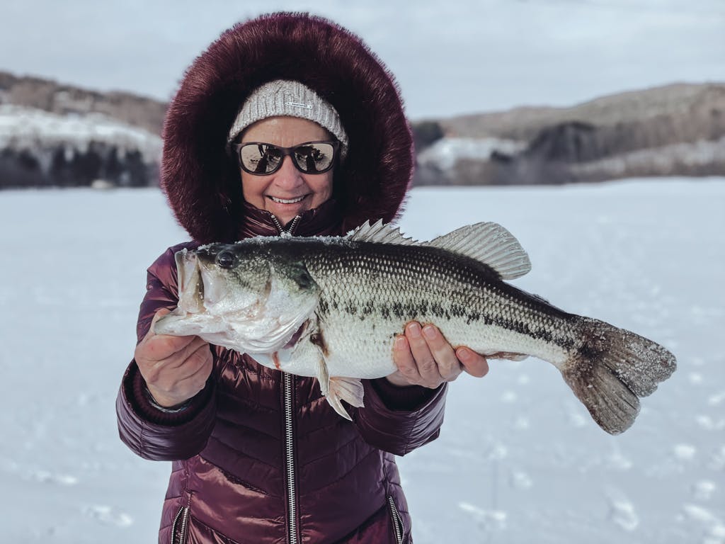 Older woman in a purple jacket holding a fish on a frozen lake while smiling