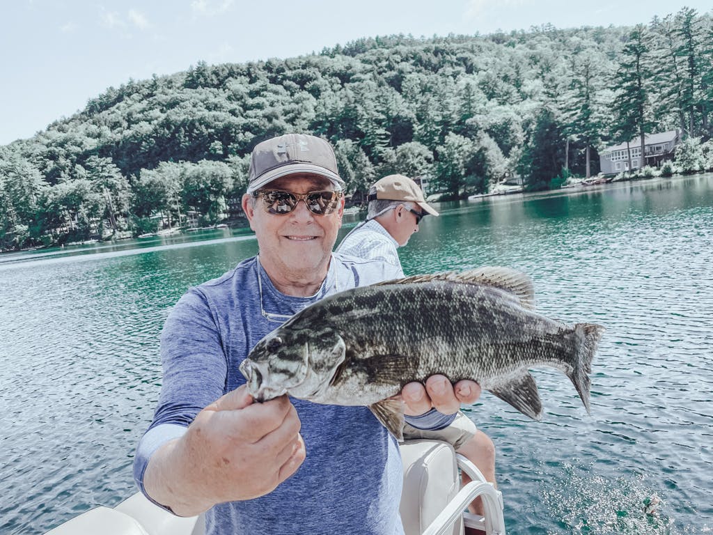 Older man in purple shirt holding a fish while smiling on a boat