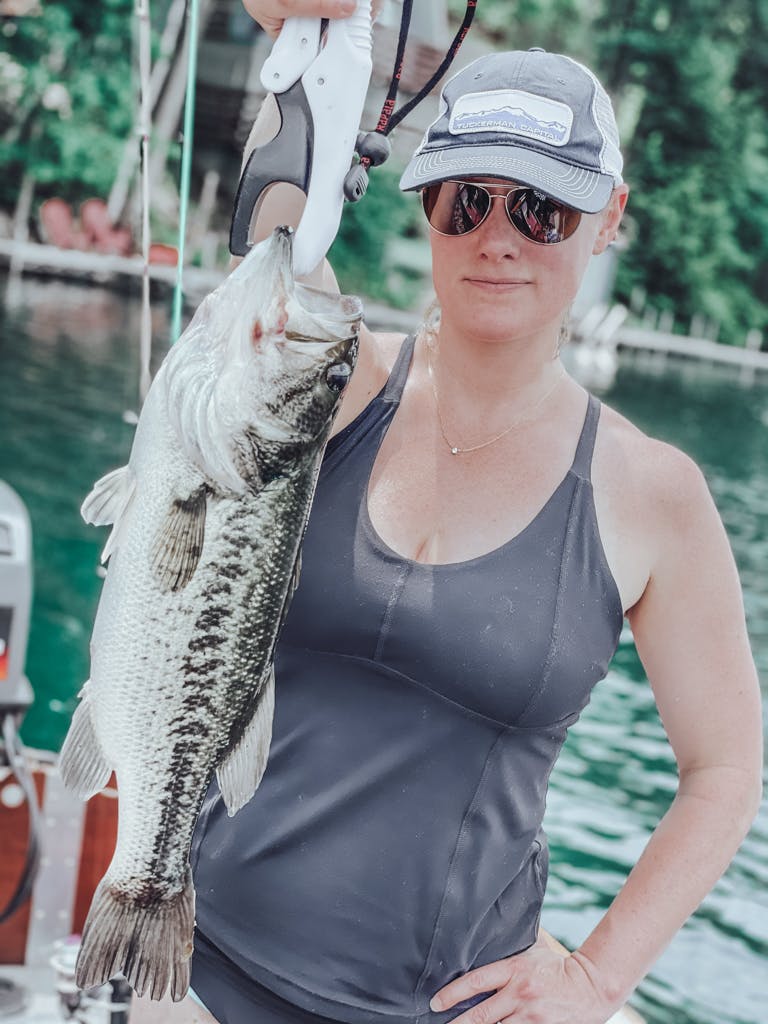 Woman in a black tank top and black and white hat holding one fish while smirking