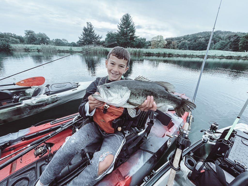 Boy wearing grey pants holding one fish while smiling in a kayak