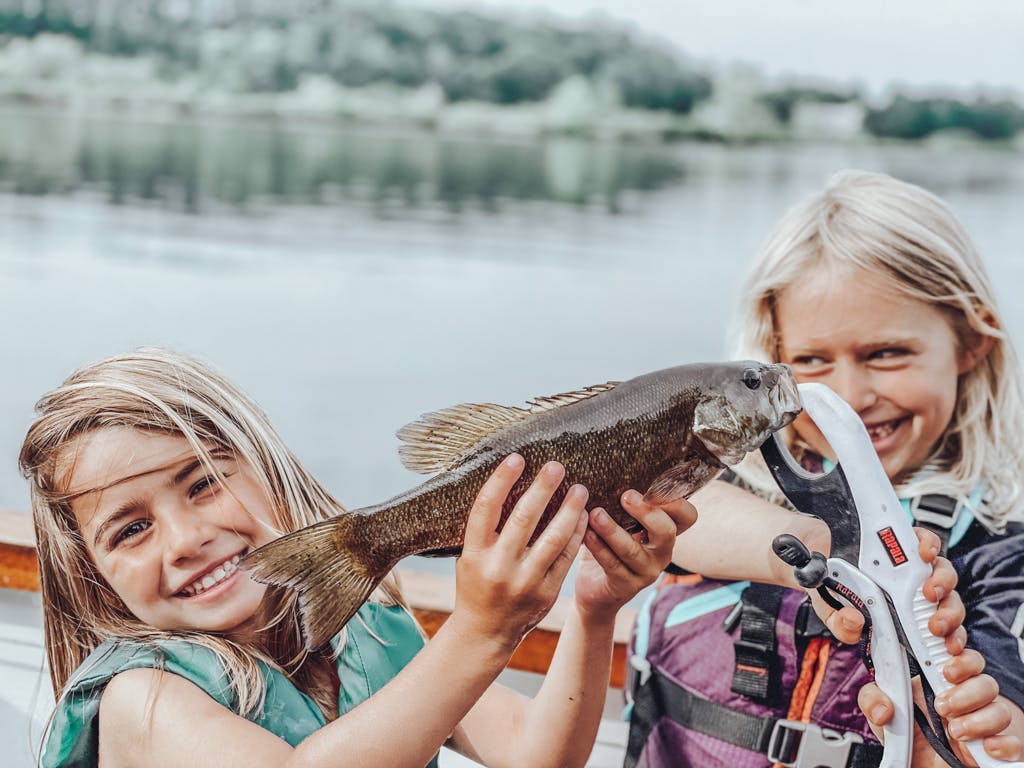 Two young girls holding one fish together while smiling in kayak