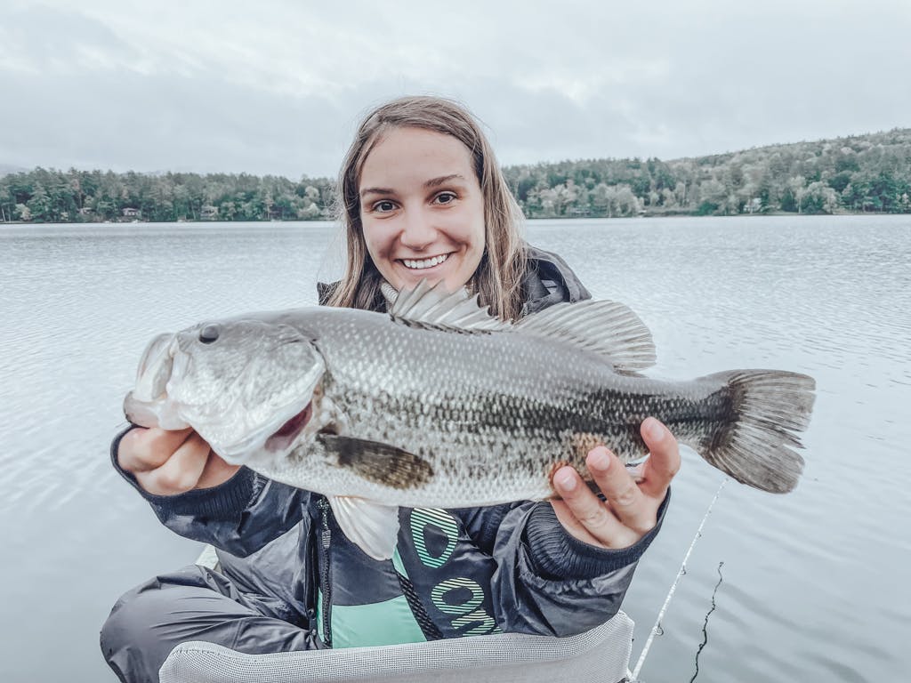 Woman in black jacket holding one fish while smiling in kayak